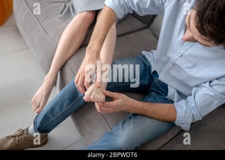 Uomo dai capelli scuri che fa massaggio ai piedi alla moglie Foto Stock