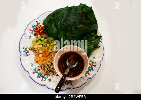 Spuntini Thai Miang Kham o un antipasto reale di involtino di foglie salate in piatto di ceramica servire con salsa dolce al caramello nel ristorante locale della Thailandia Foto Stock