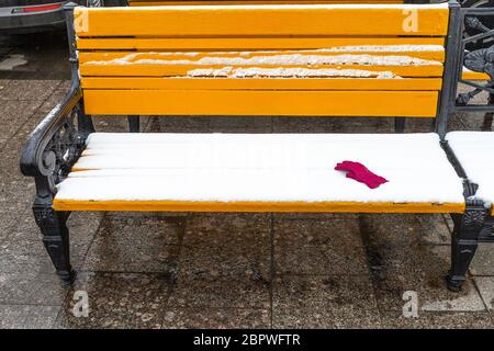 Panca di legno gialla coperta di neve con guanto femminile rosso in piazza Manezhnaya nella città di Mosca in inverno Foto Stock