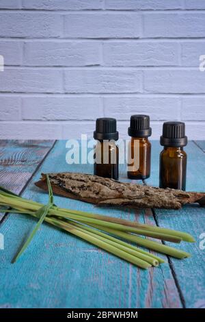 Bottiglie di olio essenziali con citronella e qualche legno su tavola di legno, pallino verticale Foto Stock