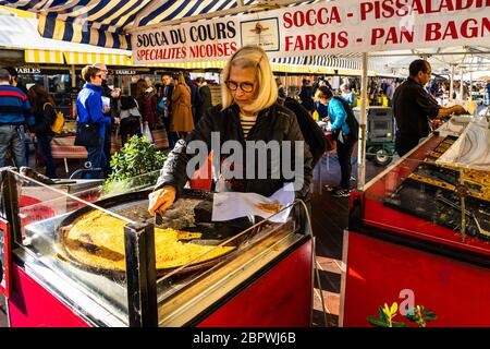 Nizza, Francia, gennaio 2020 – una donna che affetta la "socca" al mercato di Cours Saleya. La socca è una sorta di pancake a base di farina di ceci. Foto Stock