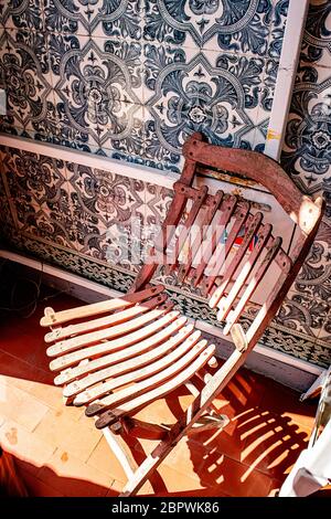 Una sedia di legno rossa si trova di fronte a una parete piastrellata blu ad Aveiro, in Portogallo Foto Stock