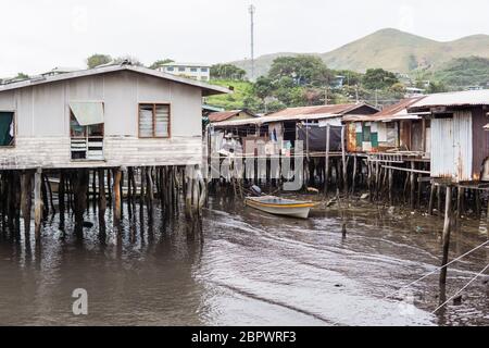 Port Moresby / Papua Nuova Guinea: Case di legno sull'acqua in villaggio galleggiante con bambini seduti nel portico Foto Stock