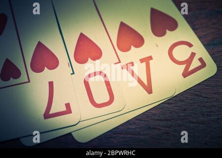 Amore, poker carte da gioco con il simbolo del cuore che formano l'amore scritto. Su una mensola di legno. Idea per biglietto di auguri per San Valentino o altro causio Foto Stock