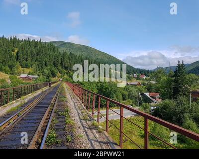 Bella strada ferroviaria di montagna a scartamento ridotto, rotaie nelle montagne dei Carpazi che attraversano la foresta nel villaggio di Vorohta, Ivano Foto Stock