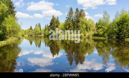 Panorama di Deixlfurter See - un piccolo lago vicino a Monaco. Paesaggio bavarese con lago, foresta e cielo azzurro e nuvoloso. Con riflessi d'acqua. Foto Stock