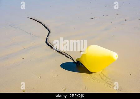 Una grande boa gialla e la sua catena di ancoraggio, utilizzata come marcatore di canale di lancio, giacente sulla sabbia bagnata a bassa marea sulla spiaggia al sole. Foto Stock