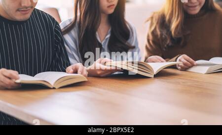 Un gruppo di giovani seduti e ci è piaciuta molto la lettura di libri insieme sul tavolo di legno Foto Stock