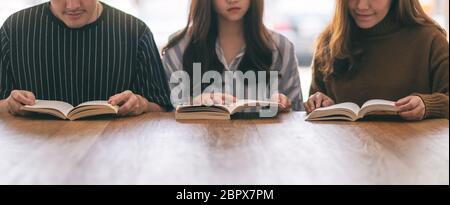 Un gruppo di giovani seduti e ci è piaciuta molto la lettura di libri insieme sul tavolo di legno Foto Stock