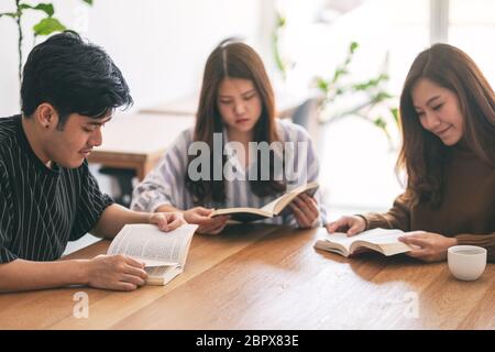 Un gruppo di giovani seduti e ci è piaciuta molto la lettura di libri insieme sul tavolo di legno Foto Stock