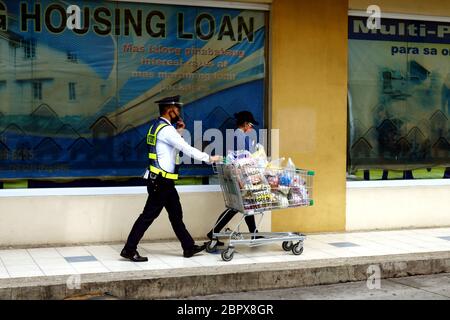 Antipolo City, Filippine - 16 maggio 2020: La guardia di sicurezza assiste un cliente spingendo il suo carrello di shopping fuori da un negozio di alimentari. Foto Stock