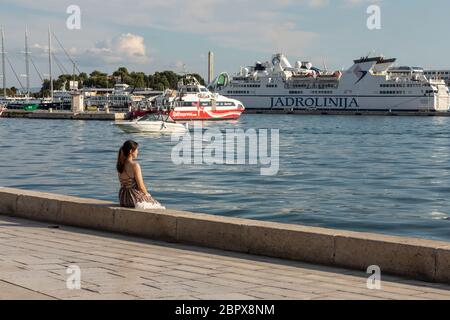 Split, Croazia, 24 settembre 2019. Una ragazza in un vestito che guarda tutte le navi da crociera che si impadono nel porto di Spalato in estate. Des. Turistico Foto Stock