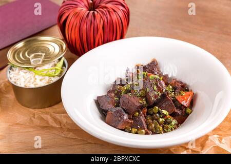 Stufato di manzo guance in salsa di vino rosso con piselli e carote, guarnita con riso bianco, servita in una piastra bianca su di un tavolo di legno. Foto Stock