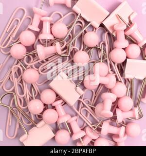 Trama composta da graffette e spille su sfondo rosa pastello. Concetto monocromatico. Foto Stock