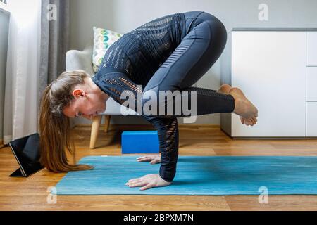 Giovane donna in posa bakasana fare yoga a casa. Allenarsi in pilates e yoga a casa Foto Stock