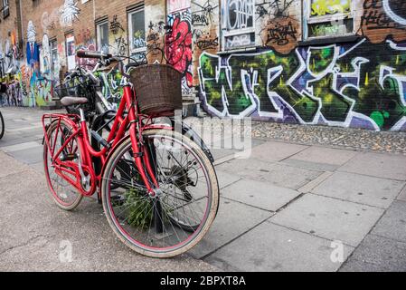 Biciclette parcheggiate in strada di fronte al muro coperto di graffiti a Shoreditch, Londra Foto Stock