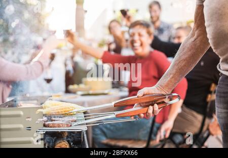 Uomo anziano cucina mais e carne al barbecue casa cena all'aperto - Chef grigliare cibo per la famiglia amici a barbecue pasto fuori - Estate stile di vita, fritte Foto Stock