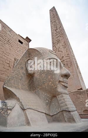 Grande statua testa di Ramses II faraone presso l'antico tempio egiziano Luxor con obelisco sullo sfondo Foto Stock