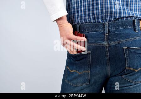 Uomo in un blue plaid shirt e jeans mette a disposizione un portafoglio in pelle nella sua tasca posteriore, sfondo bianco Foto Stock