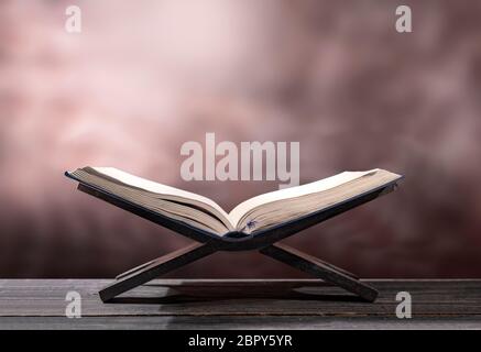 Corano aperto in cartellone in legno sul tavolo di legno su sfondo sfocato Foto Stock