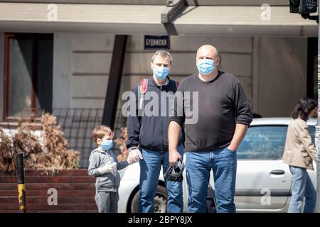 BELGRADO, SERBIA - 24 APRILE 2020: Tre persone, tra cui un padre con il bambino, che indossa una maschera respiratoria per le strade di Belgrado, d Foto Stock