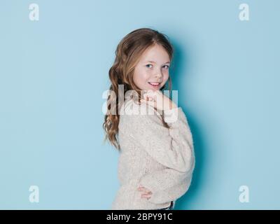 Grazioso e raffreddare 9 anno vecchia ragazza marrone con maglione di lana in posa di fronte di sfondo blu Foto Stock