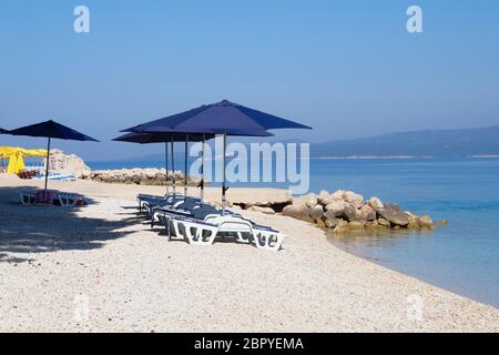 Ombrelloni e sdraio blu per rilassarsi e comfort in località balneare. Vacanze estive e viaggi per il mare. Servizio a pagamento sulle spiagge di comfort. Foto Stock