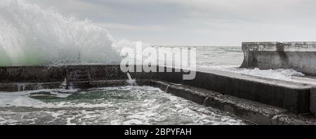 Le onde si schiantano contro il frangiflutti, formando schizzi Foto Stock