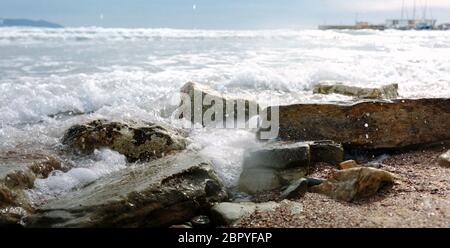 Onde schiumose rotolano sulla spiaggia rocciosa Foto Stock