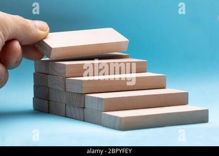 Mano d'uomo disponendo il blocco di legno come stacking passo su sfondo blu Foto Stock