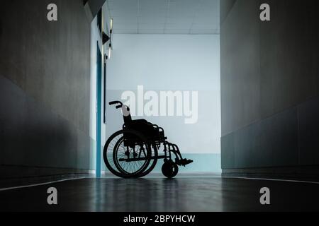 Silhouette di sedia a rotelle vuota parcheggiata nel corridoio di ospedale Foto Stock