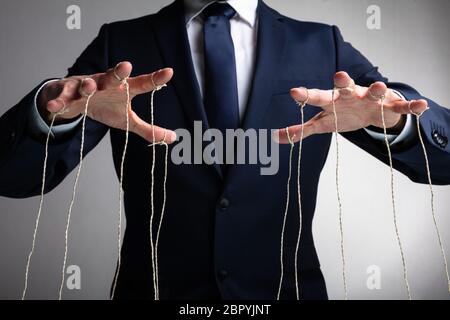Mano d'uomo controlla il fantoccio con le dita attaccata al thread contro uno sfondo grigio Foto Stock