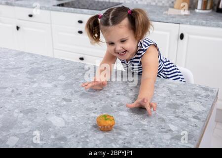 Sorridente ragazza carina la mano raggiungendo per la tortina sul banco di cucina Foto Stock