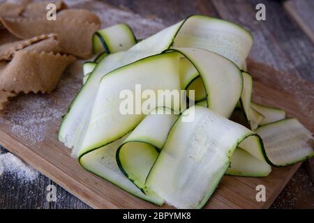 Fresco tagliato nastri di zucchine sul tagliere con pappardell fatti in casa la pasta in background. Foto Stock