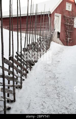 Età agricola tradizionale rosso fienile su rurale idilliaco farmland, ranch road con neve e rustico in vecchio stile in legno recinzione log in campagna, w Foto Stock