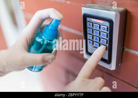 Indossare i guanti chirurgici utilizzando il disinfettante per bottiglie spray e premendo il pulsante del tastierino del codice del sistema di sicurezza. Misure preventive contro il covid-19 sulla pubblica pubblica Foto Stock