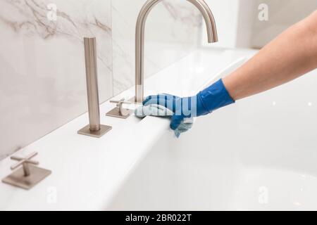 Donna in guanti lava il bagno e pulisce il rubinetto Foto Stock