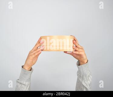 Mani femminili tenere round crivello in legno per la farina, lo sfondo grigio Foto Stock