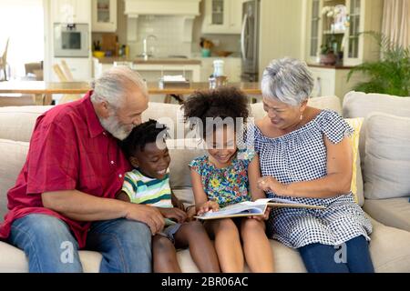 Coppia di razza mista senior seduta sul divano con il loro nipote e nipote Foto Stock