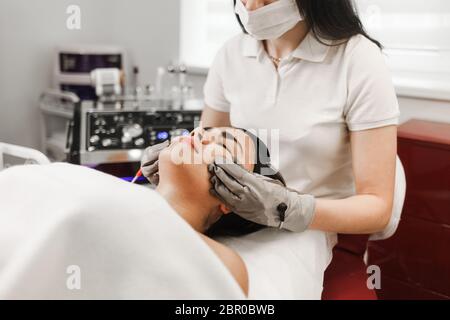 Terapia microcorrente. Cosmelotologist effettua massaggio facciale stimolante con guanti elettrici. Massaggio linfodrenante Foto Stock