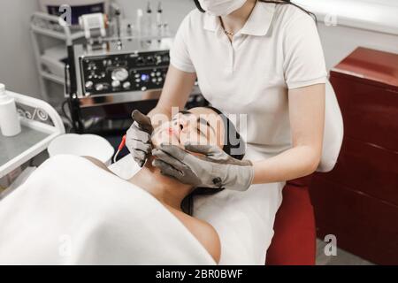 Terapia microcorrente. Cosmelotologist effettua massaggio facciale stimolante con guanti elettrici. Massaggio linfodrenante Foto Stock