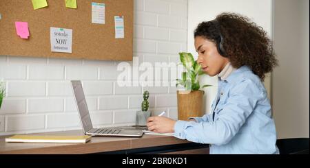 Studente africano teen girl indossa le cuffie guardando il webinar in classe facendo appunti. Foto Stock