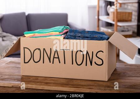 Close-up di vestiti in donazione casella sulla scrivania in legno Foto Stock