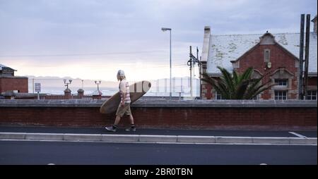 Surfista maschio caucasico che indossa abiti casual che tengono una tavola da surf in legno e wallkind Foto Stock