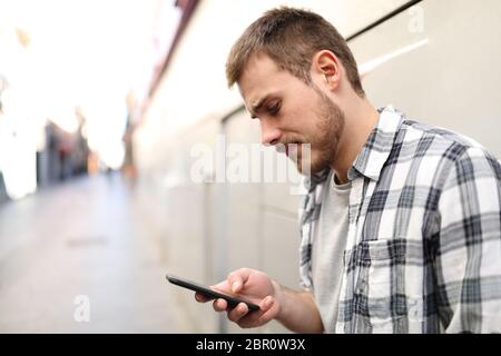 Vista laterale verticale di un triste uomo in un lonely street utilizzando uno smart phone Foto Stock