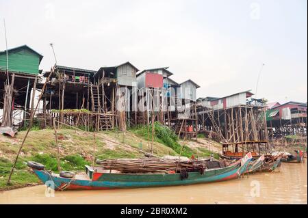 Barche sul fiume con case su palafitte sullo sfondo a Kampong Phluk, Siem Reap Provincia, Nord-centrale Cambogia, Sud-Est asiatico Foto Stock