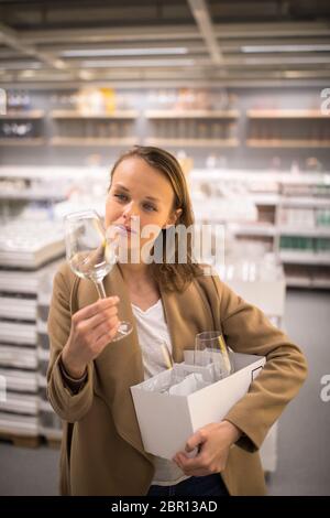 Piuttosto, giovane donna in una home negozio di fornitura per la scelta del giusto bicchieri per il suo vino tossicodipendenza (toni di colore immagine; shallow DOF) Foto Stock