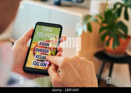 primo piano di un giovane caucasico, vestendo abiti casual, seduto comodamente in una poltrona interna, con lo smartphone in mano con il testo Foto Stock