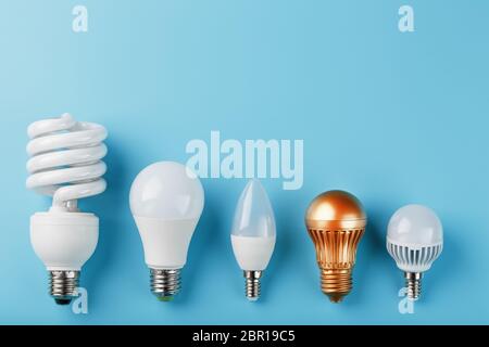 Una lampadina dorata in una fila di lampade bianche a risparmio energetico su sfondo blu. Vista dall'alto Foto Stock