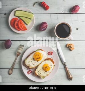 La colazione brinda con verdure e uova fritte su piastra bianca, una tazza di caffè e un po' di frutta su sfondo di legno. Cibo sano concetto. Vista da una Foto Stock